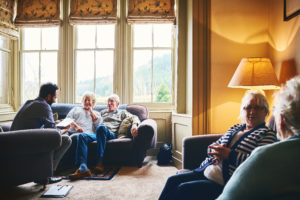 Doctor visiting a care home and talking with elderly couple sitting on couch